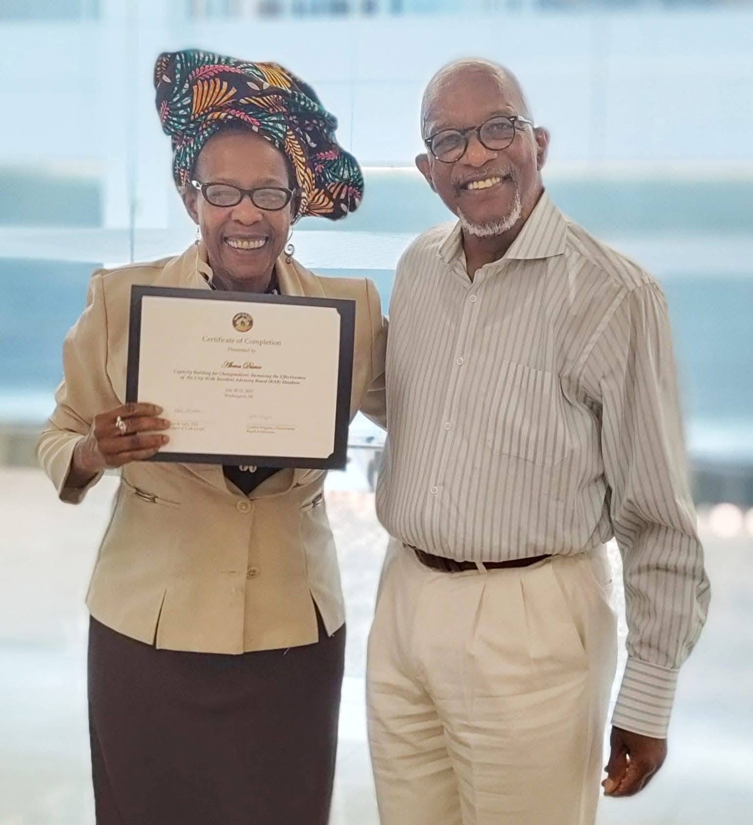 Abena Disroe smiling in a colorful headwrap, holding a certificate of completion